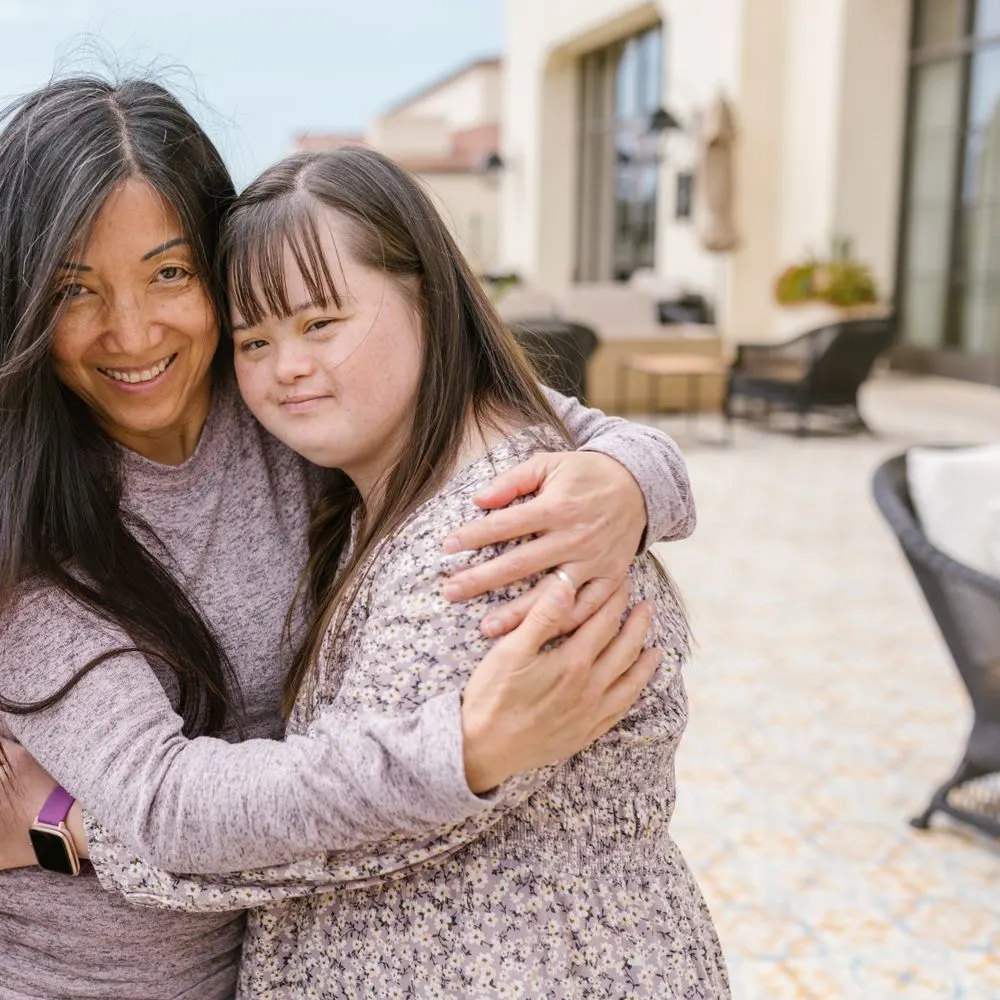 A mother and her adult daughter, who has Down syndrome, embracing outdoors