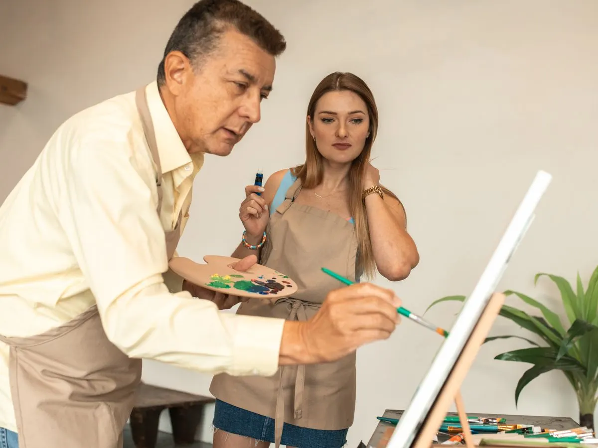 Two adults painting at an easel together in a bright studio
